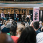 Image shows a group of people listening to speakers seated on a stage with a ChurchWorks banner on display on the right