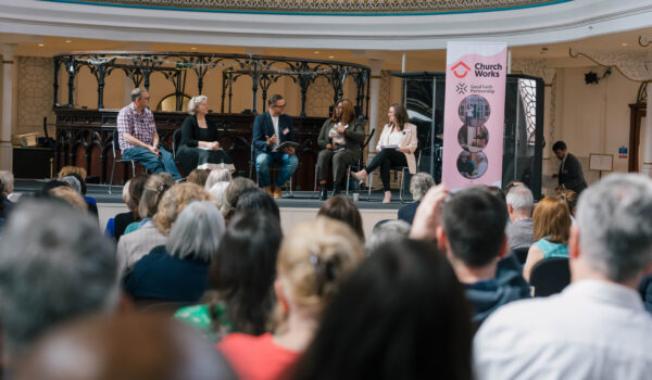 Image shows a group of people listening to speakers seated on a stage with a ChurchWorks banner on display on the right