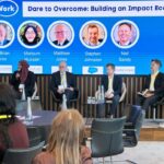 Image shows a group of people seated on a platform with a screen behind them saying Faith At Work Dare to Overcome: Building An Impact Economy