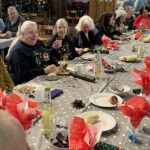 Image shows people seated at tables inside a church at Christmas time, about to enjoy a festive meal