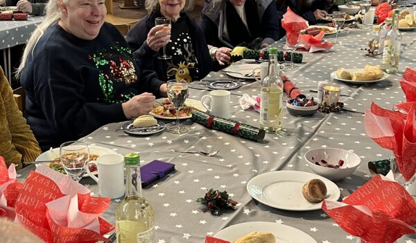 Image shows people seated at tables inside a church at Christmas time, about to enjoy a festive meal
